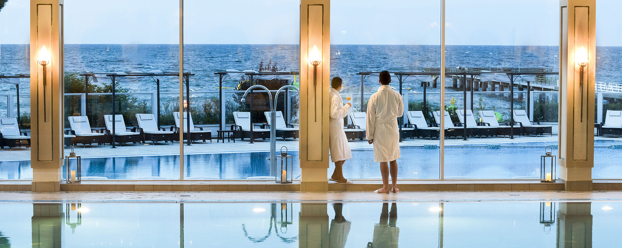 Innenpool mit Meerblick im Maritim Seehotel Timmendorfer Strand, zwei Gäste in Bademänteln am Fenster.