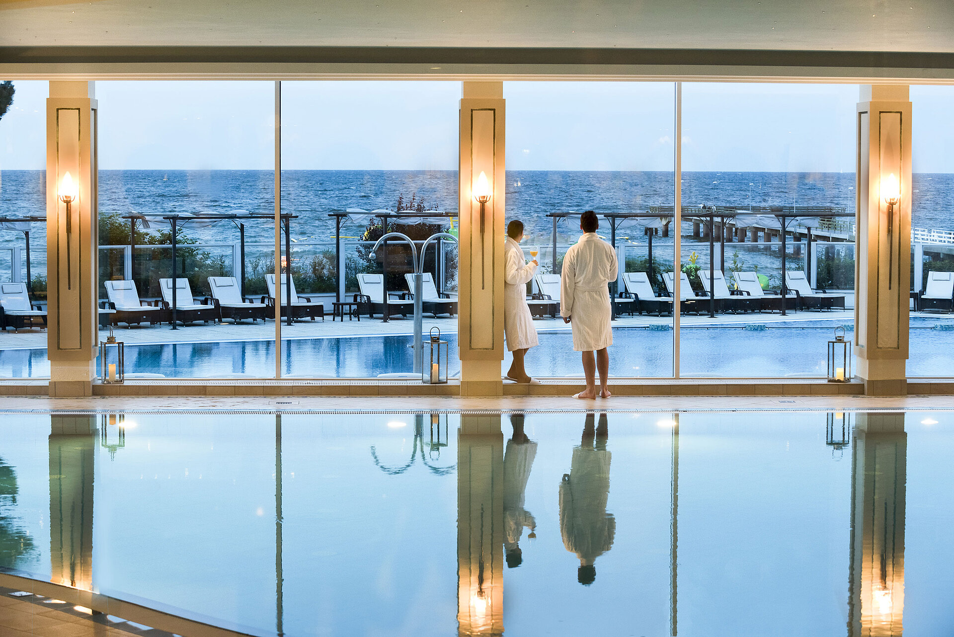 Schwimmbad Innenpool mit Meerblick im Maritim Seehotel Timmendorfer Strand, zwei Gäste in Bademänteln am Fenster.