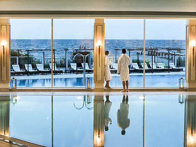 Schwimmbad Innenpool mit Meerblick im Maritim Seehotel Timmendorfer Strand, zwei Gäste in Bademänteln am Fenster.