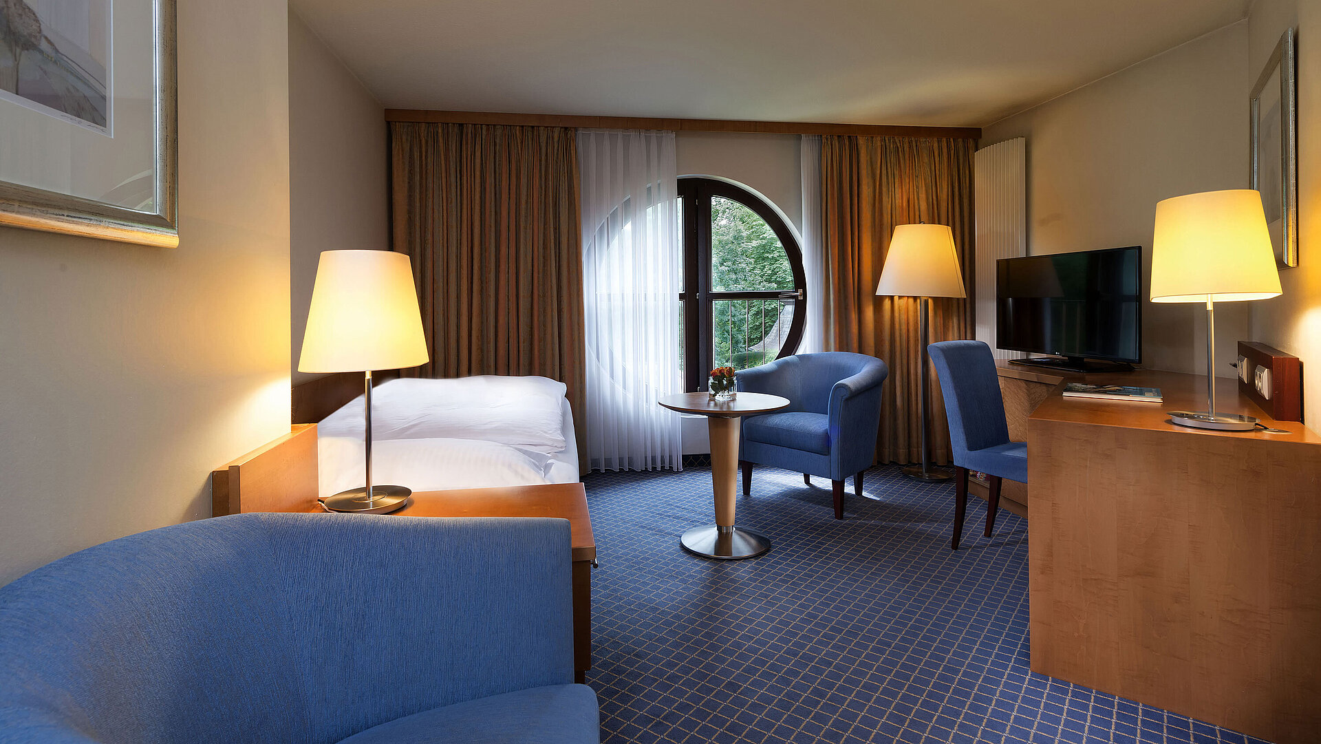 Classic Zimmer im Maritim Hotel Fulda mit Einzelbett, Schreibtisch, Sitzbereich und rundem Fenster mit Ausblick.