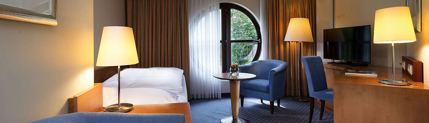 Classic Zimmer im Maritim Hotel Fulda mit Einzelbett, Schreibtisch, Sitzbereich und rundem Fenster mit Ausblick.