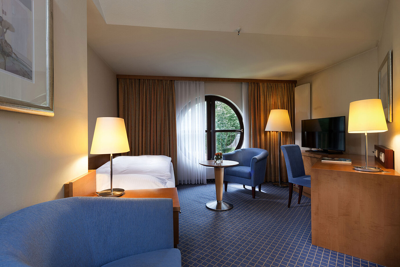 Classic Zimmer im Maritim Hotel Fulda mit Einzelbett, Schreibtisch, Sitzbereich und rundem Fenster mit Ausblick.