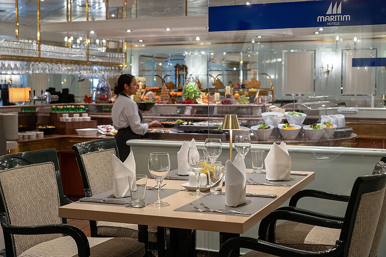 Restaurant Maritim Restaurantbereich mit gedecktem Tisch, Buffetstation im Hintergrund und Servicekraft im Maritim Hotel.