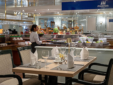 Restaurantbereich mit gedecktem Tisch, Buffetstation im Hintergrund und Servicekraft im Maritim Hotel.