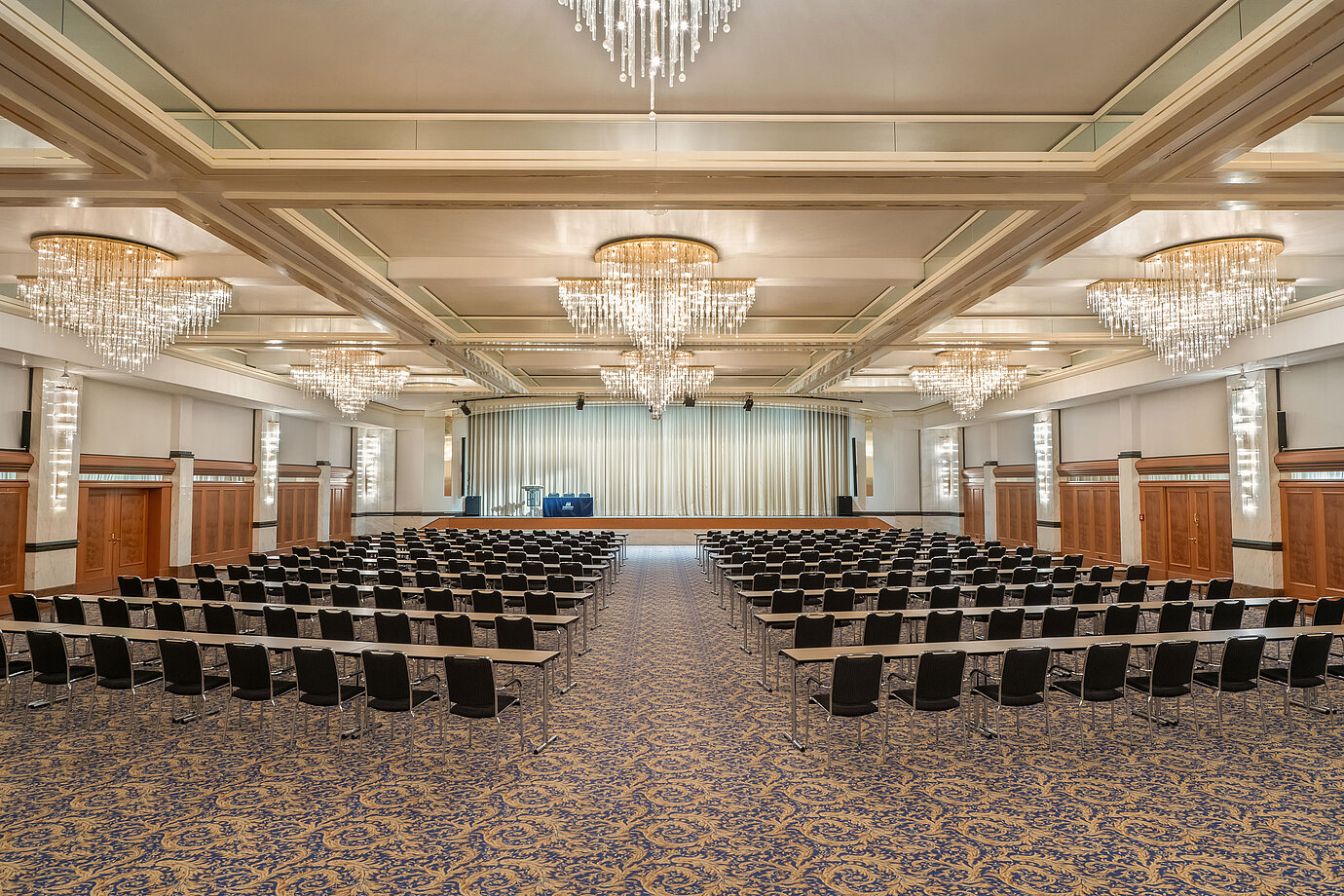 Fürst-von-Metternich-Saal mit großer Bühne, Reihenbestuhlung, eleganten Kronleuchtern und hellem Ambiente.