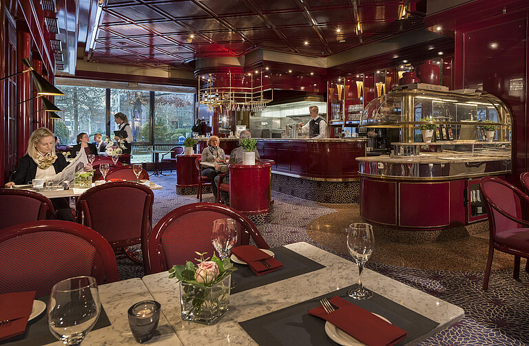 Das Bild zeigt das gemütliche Café "Brasserie" im Maritim Hotel Bonn mit roter Einrichtung und entspanntem Ambiente.