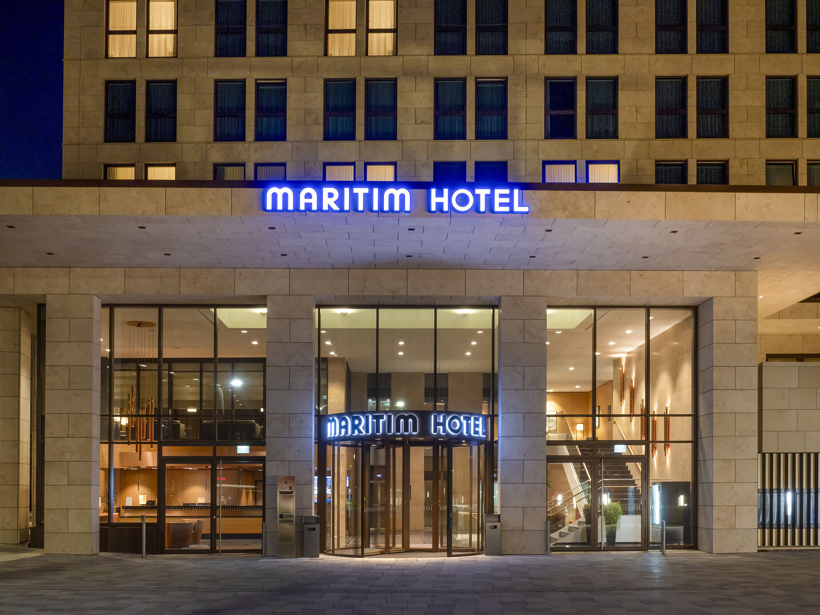 Beleuchteter Eingang des Maritim Hotel Ingolstadt mit moderner Glasfassade bei Nacht.