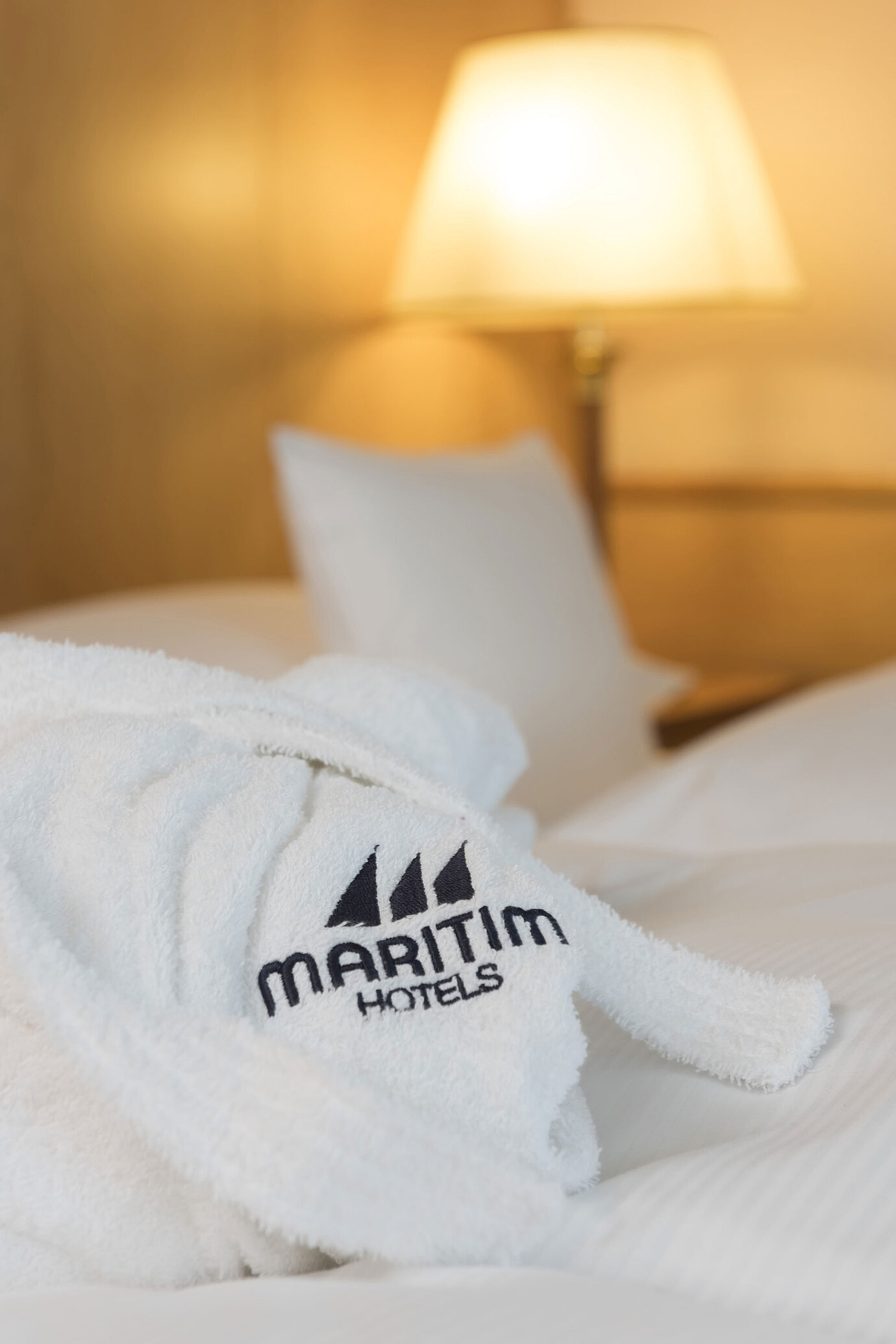 Weicher Bademantel mit Maritim Hotels Logo auf einem frisch gemachten Bett im Hotelzimmer