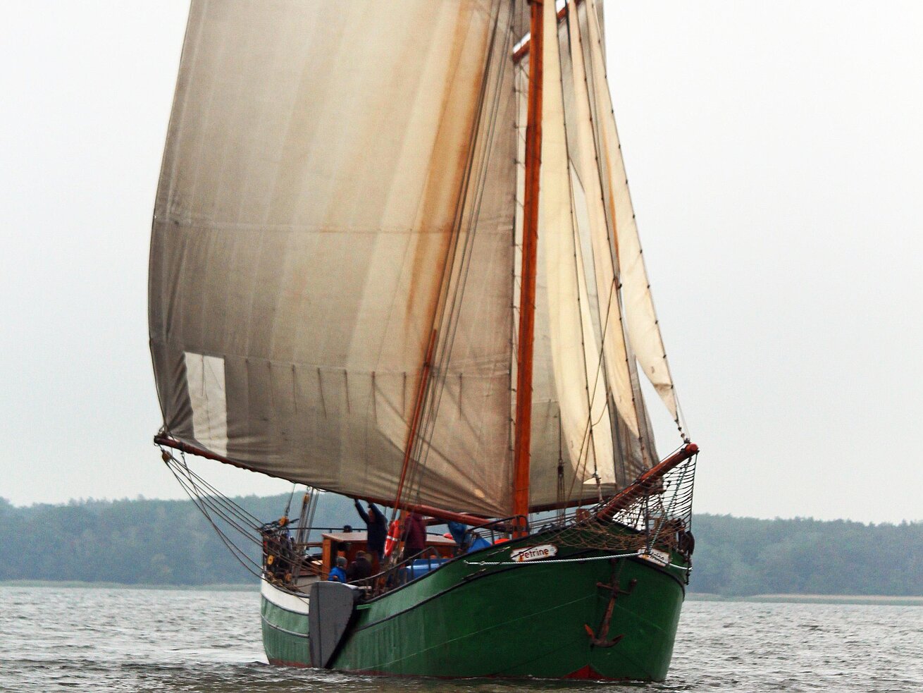 Ein traditionelles Segelschiff mit grünem Rumpf und gesetzten Segeln fährt auf dem Wasser.
