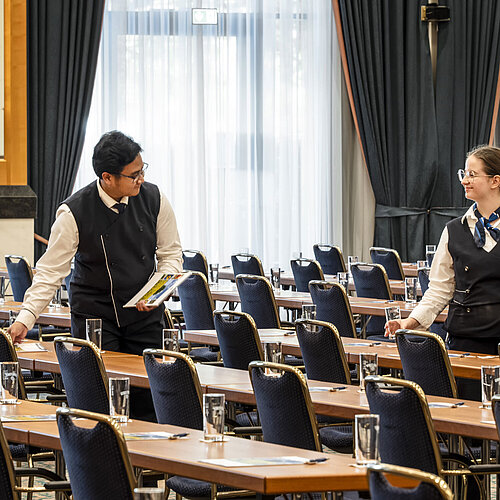 Mitarbeiter des Maritim Hotel Magdeburg beim Vorbereiten des Saals mit Gläsern und Unterlagen auf den Tischen.