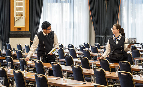 Mitarbeiter des Maritim Hotel Magdeburg beim Vorbereiten des Saals mit Gläsern und Unterlagen auf den Tischen.