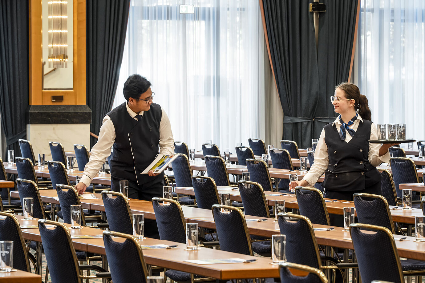 Mitarbeiter des Maritim Hotel Magdeburg beim Vorbereiten des Saals mit Gläsern und Unterlagen auf den Tischen.