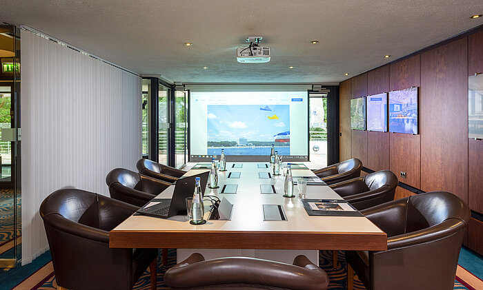 Konferenzraum „Salon Fulda“ im Maritim Hotel Timmendorfer Strand mit Konferenztisch, Ledersesseln und Projektor.