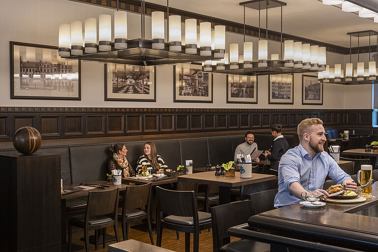 Gäste genießen Speisen im gemütlichen Restaurant "Rheinische Stov" des Maritim Hotel Düsseldorf mit stilvollem Interieur.