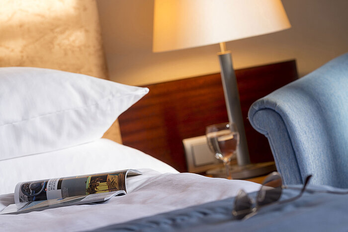 Detailaufnahme eines Hotelzimmers im Maritim Hotel Fulda mit Bett, Zeitschrift, Brille und Glas Wasser auf dem Nachttisch.