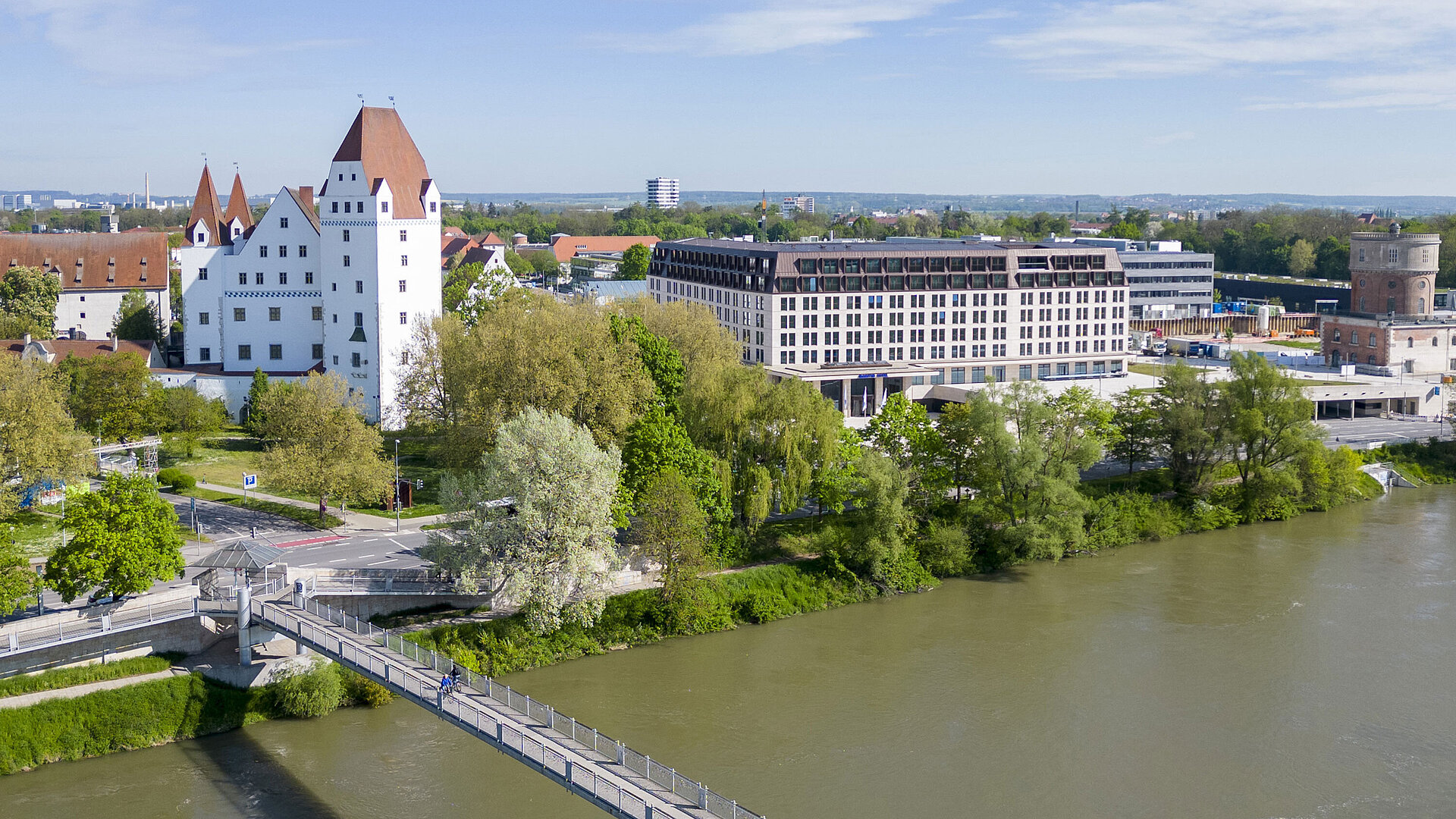 Außenansicht Luftaufnahme des Maritim Hotel Ingolstadt mit Blick auf die Donau, eine Fußgängerbrücke und das historische Schloss.