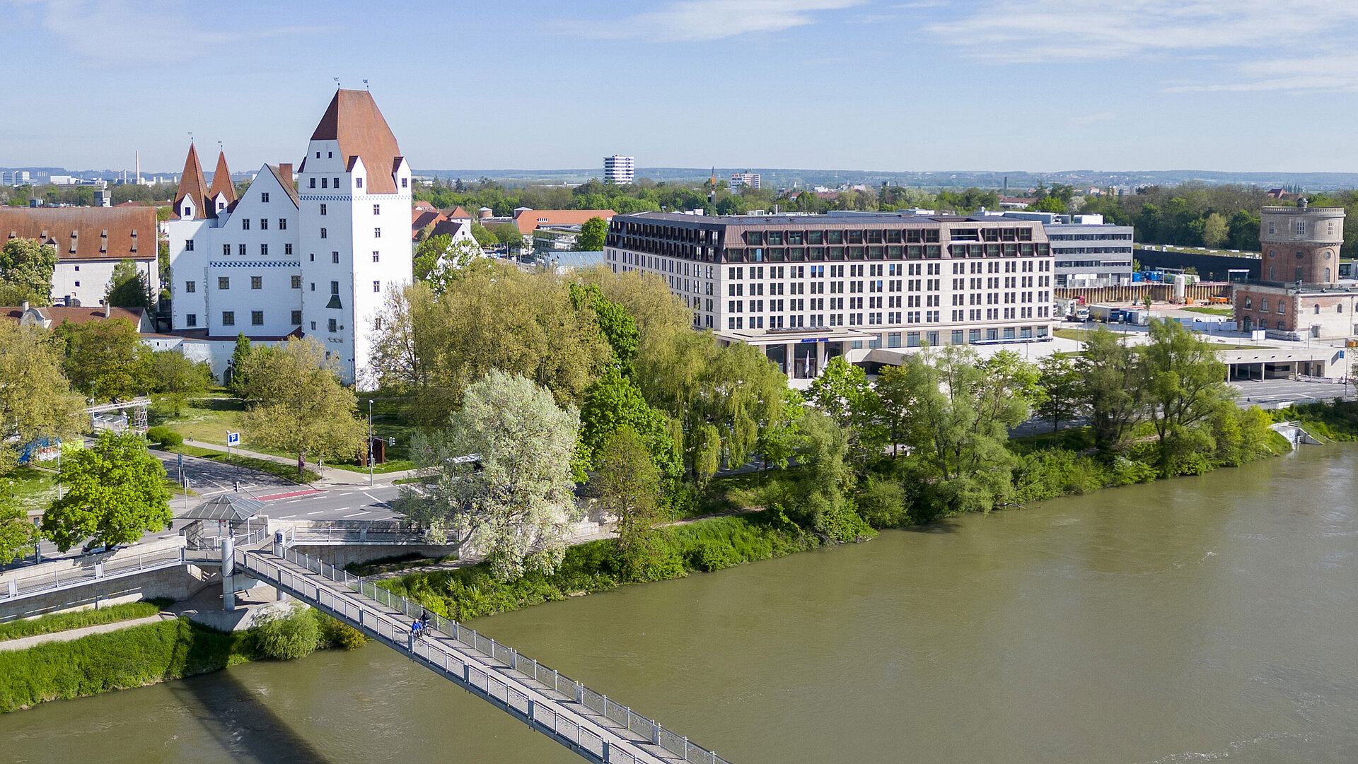 Außenansicht Luftaufnahme des Maritim Hotel Ingolstadt mit Blick auf die Donau, eine Fußgängerbrücke und das historische Schloss.