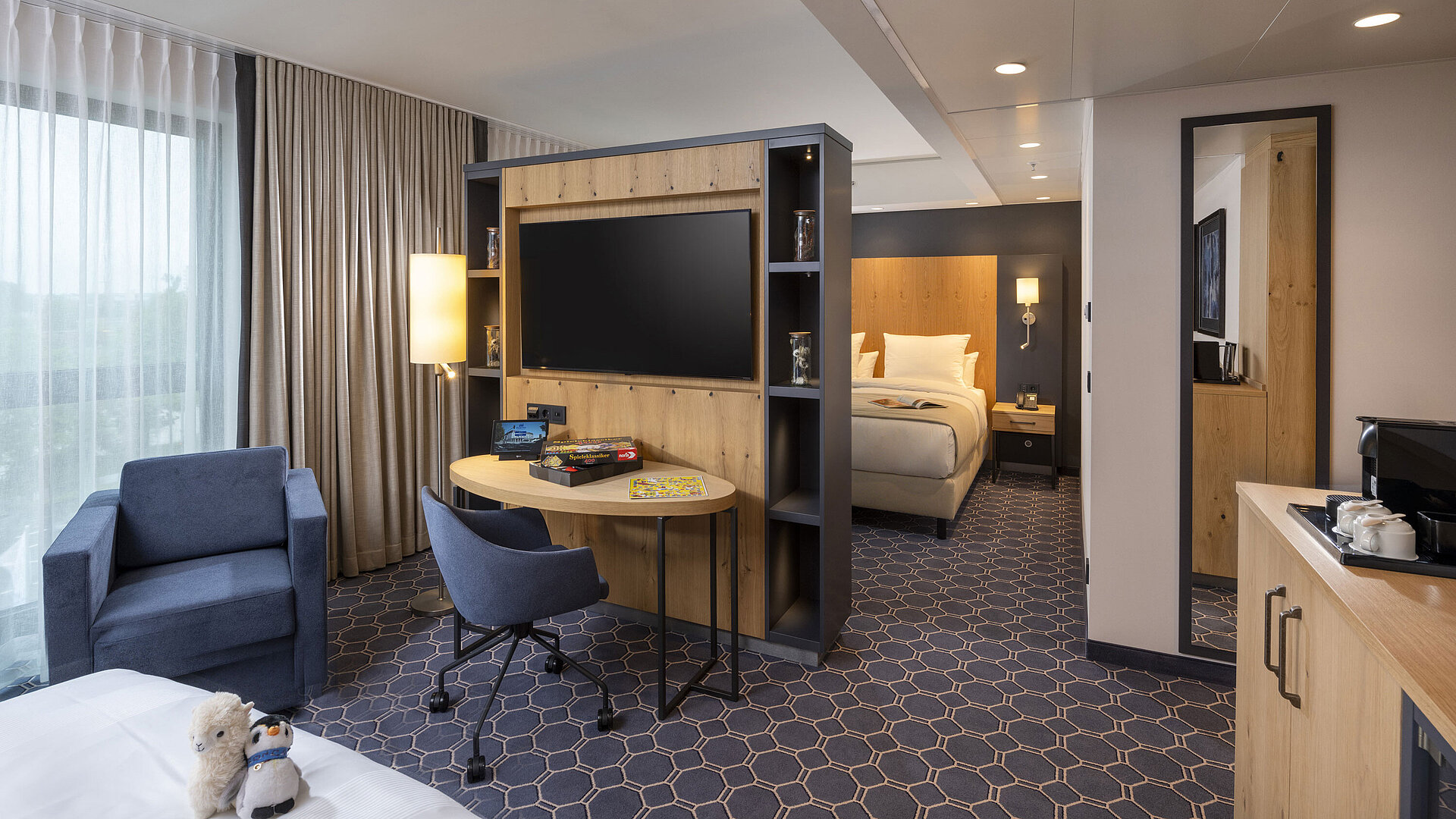 Familiensuite Helles Zimmer im Maritim Hotel Ingolstadt mit Sitzecke, Schreibtisch, großem TV und Blick auf die grüne Umgebung.