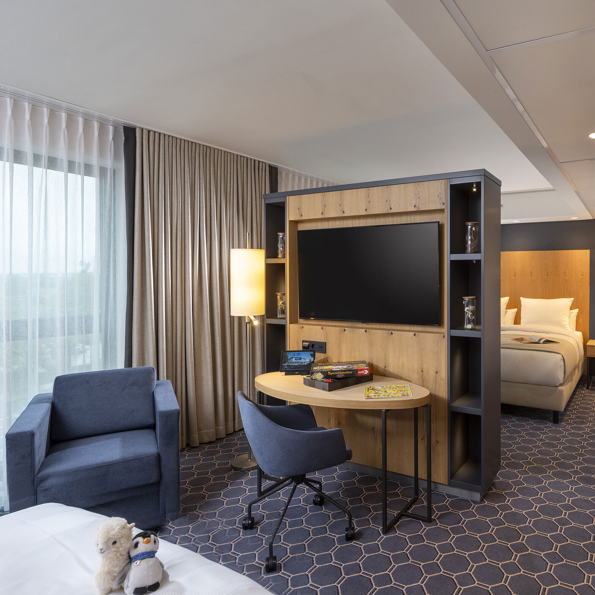 Familiensuite Helles Zimmer im Maritim Hotel Ingolstadt mit Sitzecke, Schreibtisch, großem TV und Blick auf die grüne Umgebung.