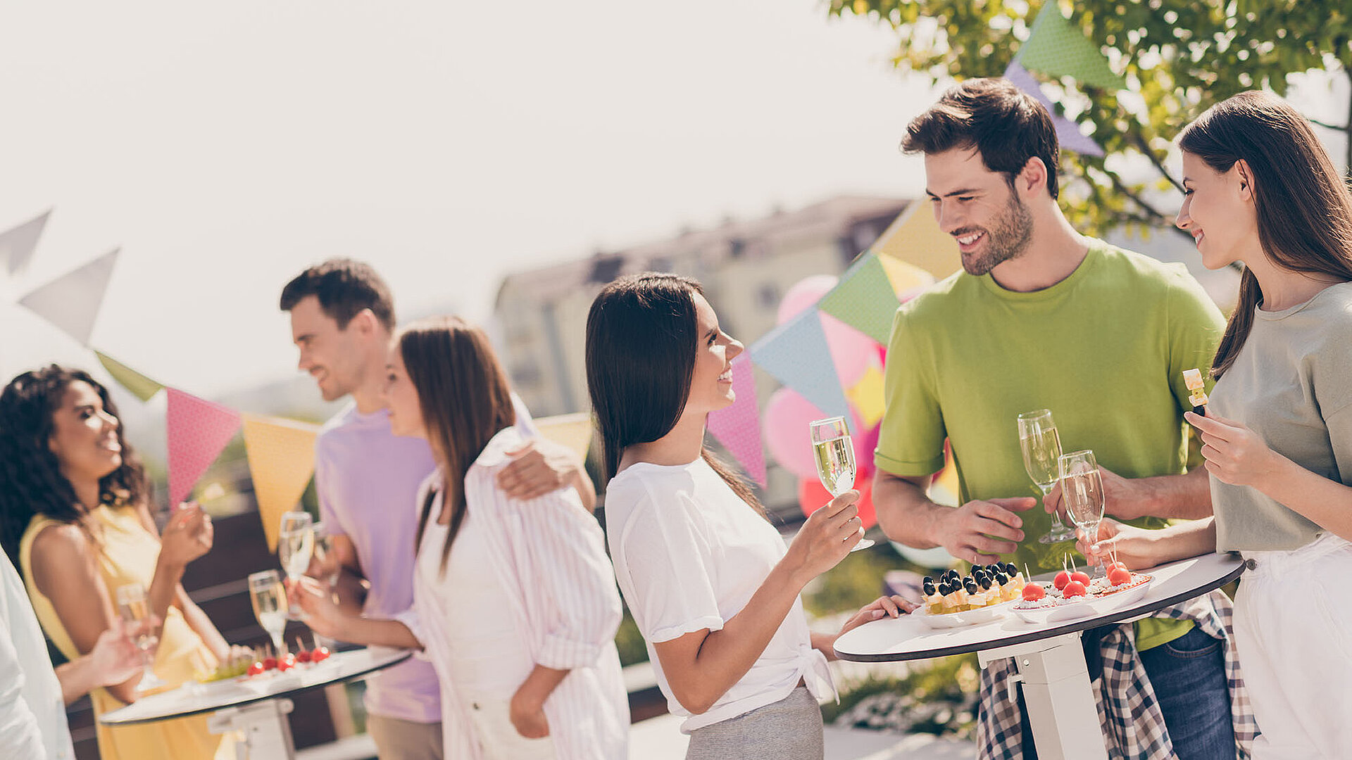 Menschen unterhalten sich fröhlich bei einer Gartenparty mit Snacks und Sekt