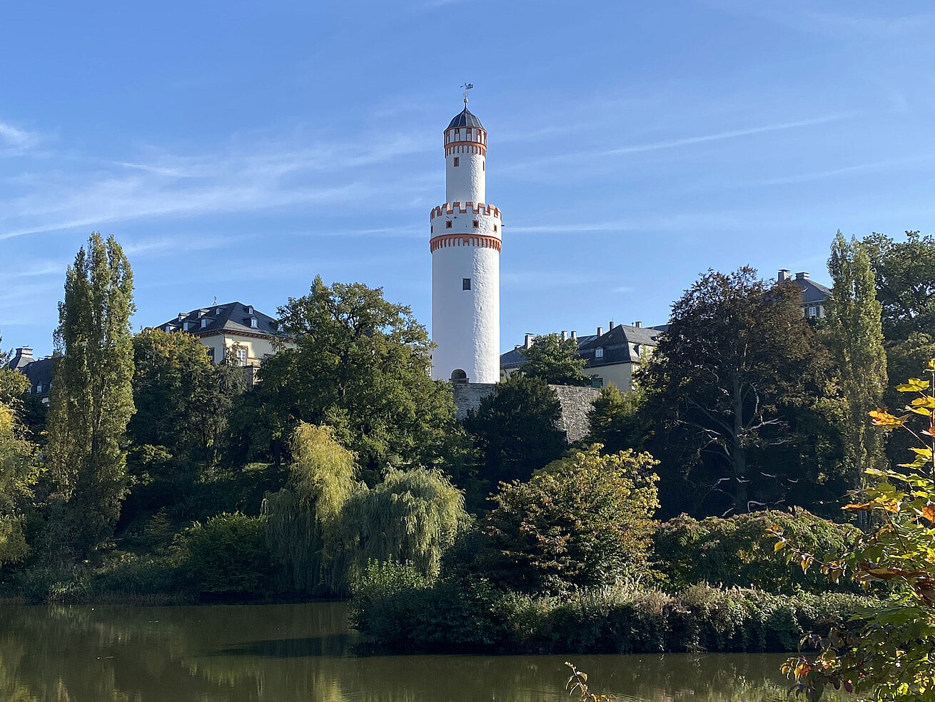 Weißer Turm in Bad Homburg vor blauem Himmel und umgeben von grüner Natur.