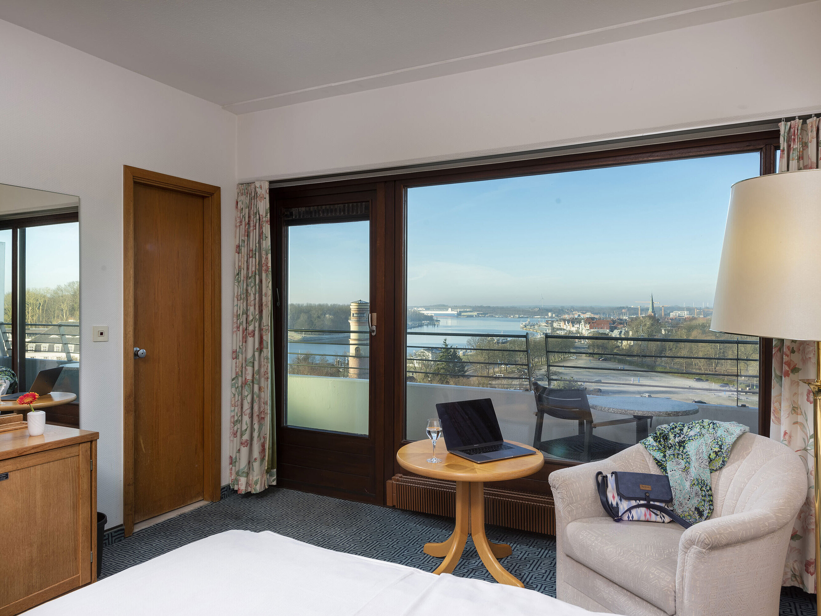 Helles Hotelzimmer mit Balkon, Schreibtisch und Ausblick auf die Trave und die Lübecker Bucht
