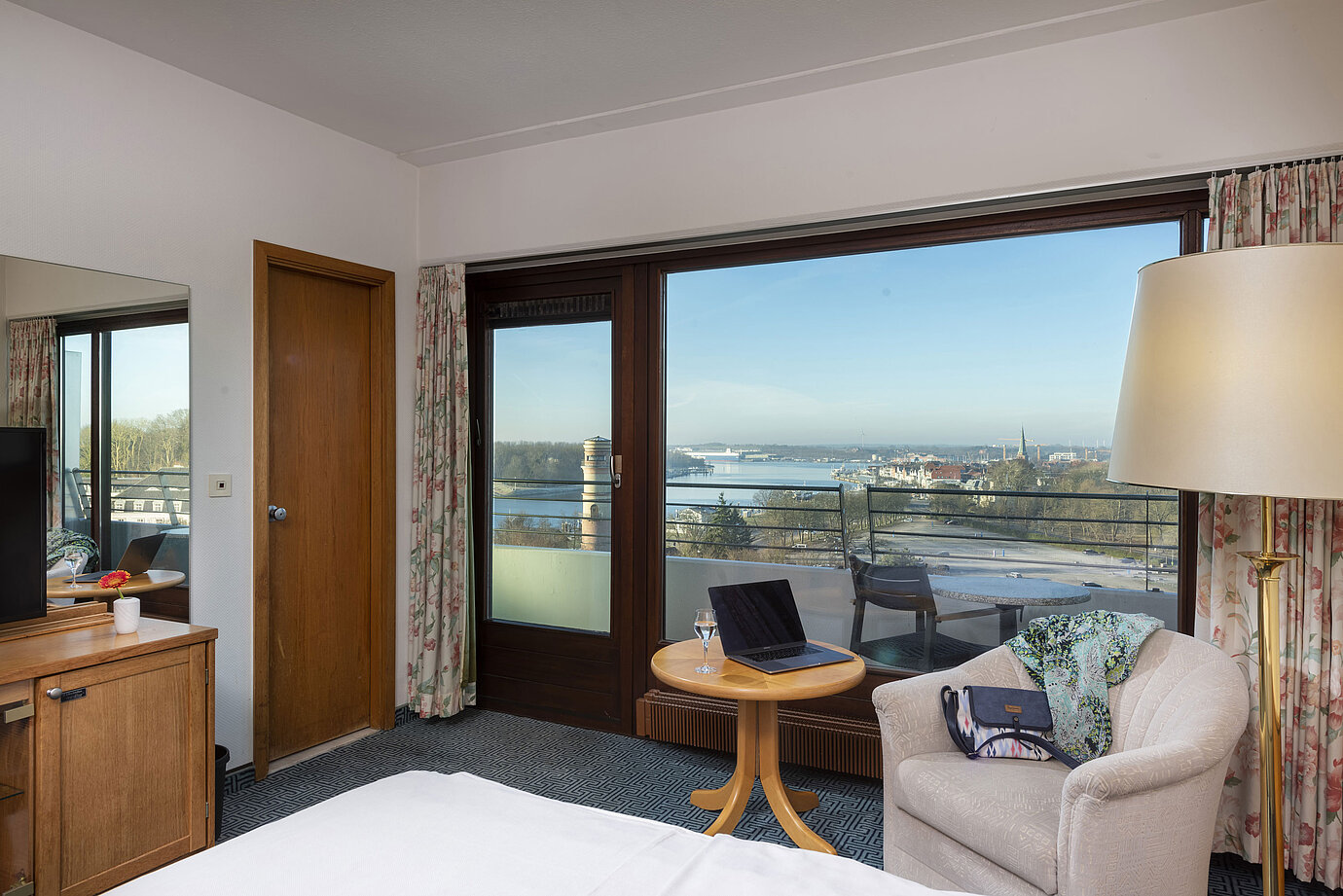 Helles Hotelzimmer mit Balkon, Schreibtisch und Ausblick auf die Trave und die Lübecker Bucht