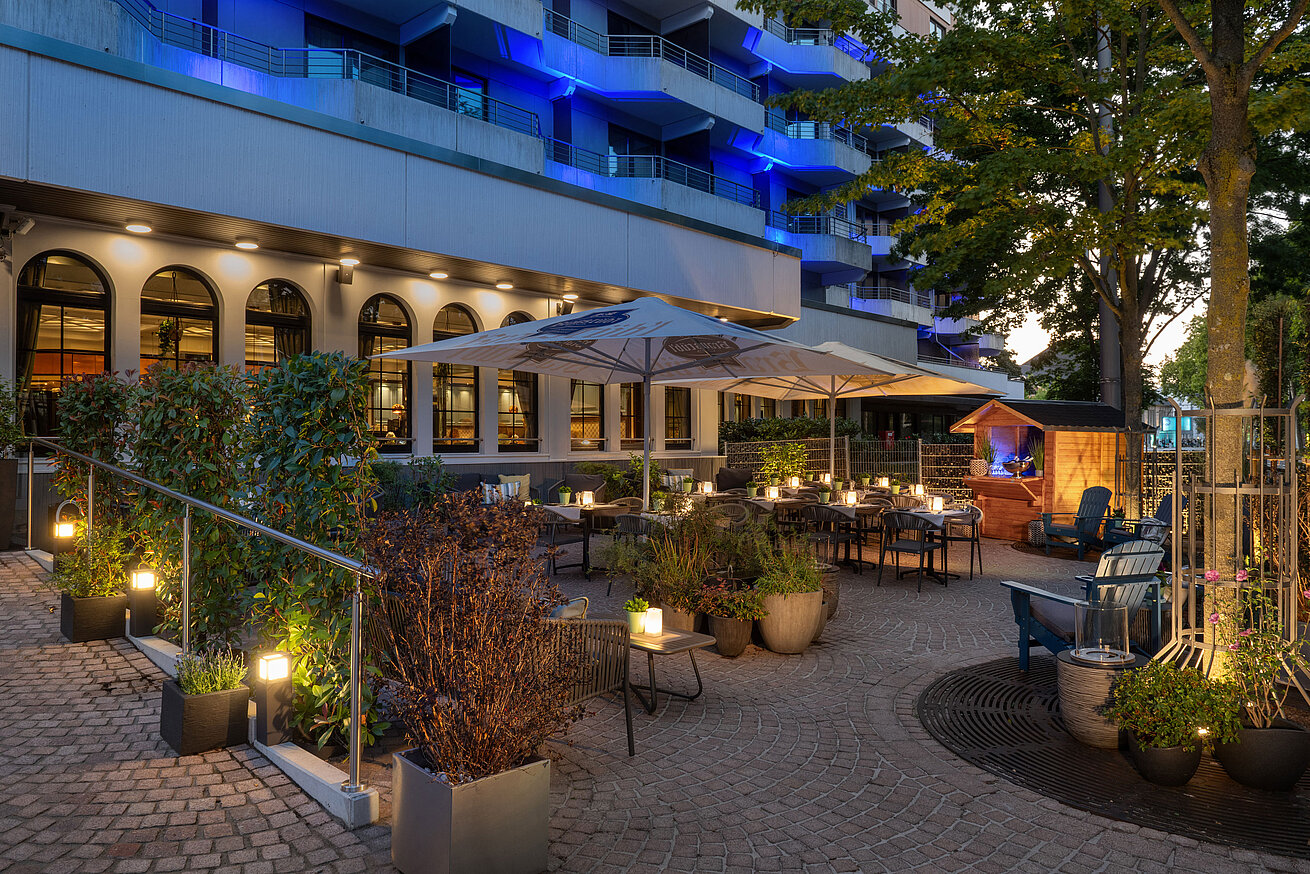 Beleuchtete Außenterrasse des Restaurants mit Sitzplätzen und Bäumen am Abend