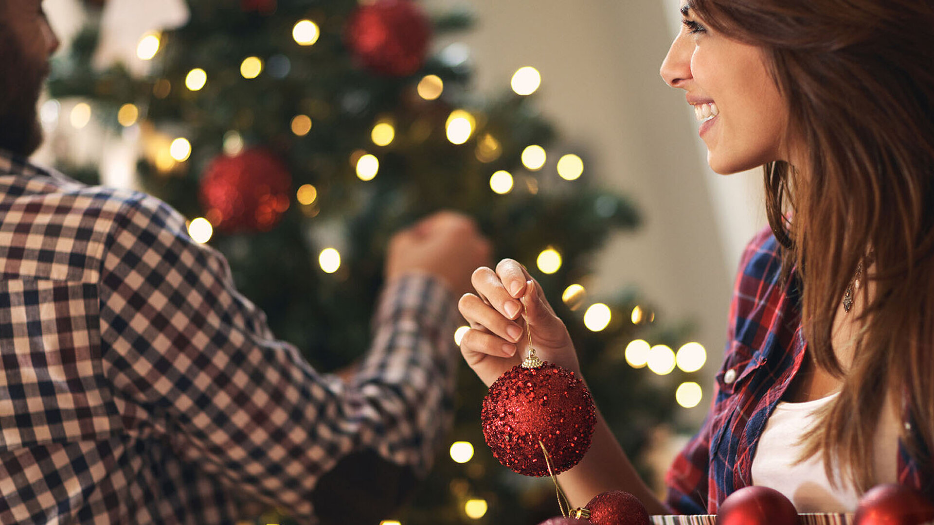 © luckybusiness - AdobeStock.com Frau schmückt Weihnachtsbaum mit roten Kugeln und Lichtern