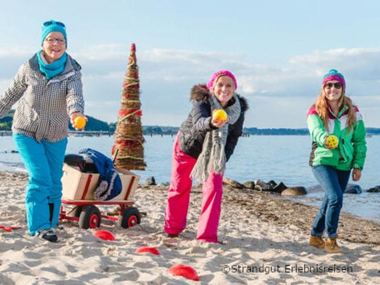 Drei Frauen stehen am winterlichen Ostseestrand und werfen mit Bossel Kugeln.