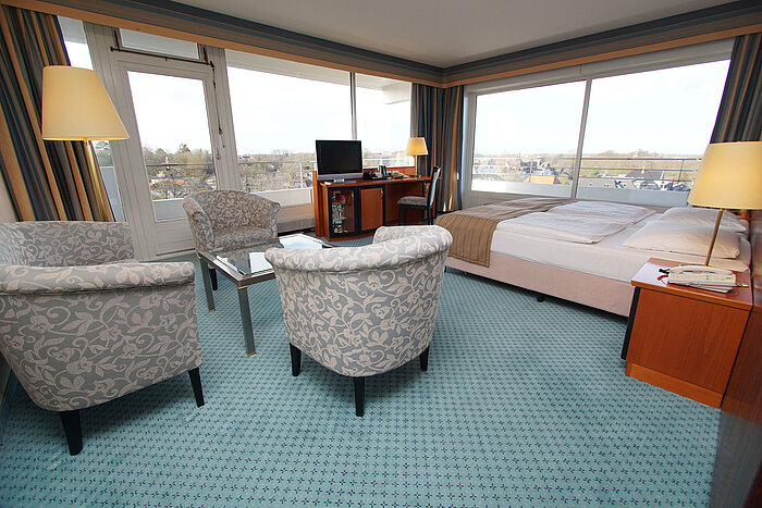 Comfort Zimmer im Maritim Hotel Kiel, mit Sitzbereich, Schreibtisch, Doppelbett und großen Fenstern mit Blick auf die Stadt.
