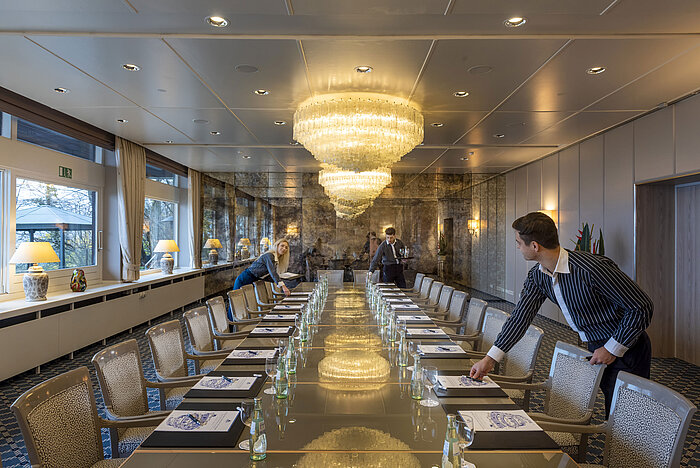 Salon Oslo im Maritim Hotel Kiel, eleganter Konferenzraum mit Kronleuchtern und langer Tischreihe, Personal richtet den Raum ein.
