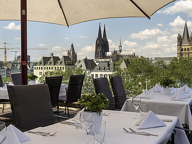 Dachterrasse des Maritim Hotels Köln mit Blick auf den Rhein und die Hohenzollernbrücke, gedeckte Tische unter Sonnenschirmen
