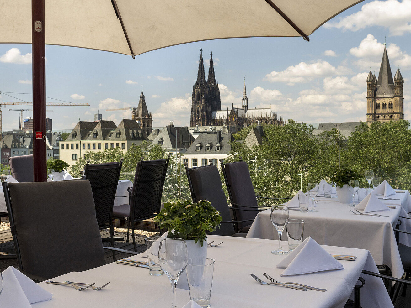 Dachterrasse des Maritim Hotels Köln mit Blick auf den Rhein und die Hohenzollernbrücke, gedeckte Tische unter Sonnenschirmen
