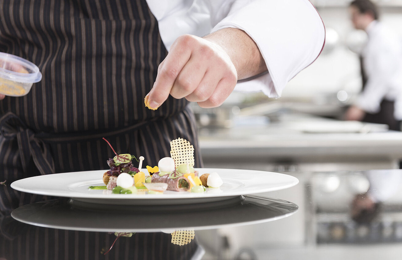 Koch richtet ein Gourmetgericht mit Gemüse, Kräutern und kunstvollen Elementen in der Orangerie an.