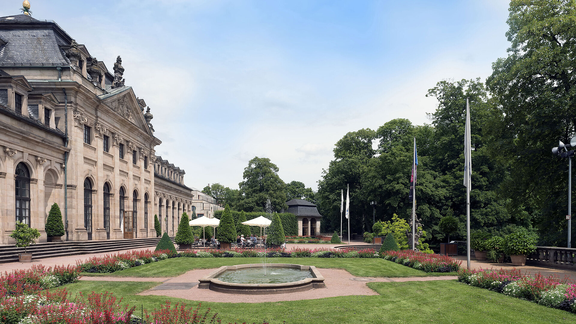 Außenansicht Die barocke Orangerie Fulda mit blühendem Garten, Terrasse und historischem Pavillon im Hintergrund.