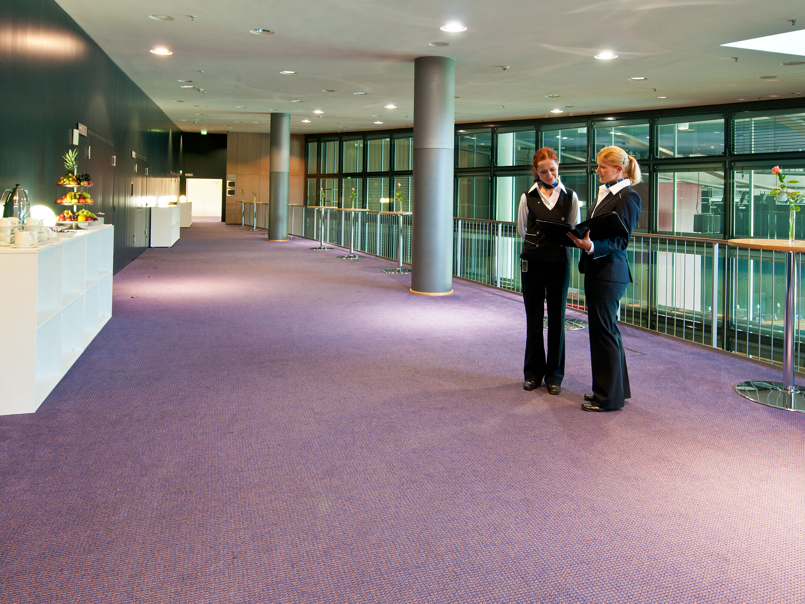  Foyer im Maritim Hotel Dresden mit zwei Mitarbeitenden in Uniform, Stehtischen und einer Obststation.
