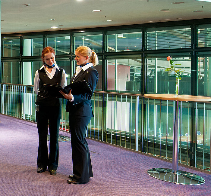  Foyer im Maritim Hotel Dresden mit zwei Mitarbeitenden in Uniform, Stehtischen und einer Obststation.