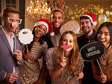 © Monkey Business - AdobeStock.com Elegante Gruppe bei festlicher Weihnachtsfeier mit Sekt und Weihnachtsmützen vor goldenem Hintergrund