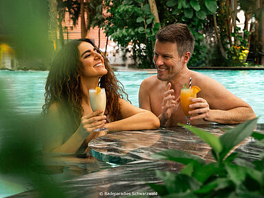 Paar entspannt im Pool mit Cocktails in tropischer Umgebung