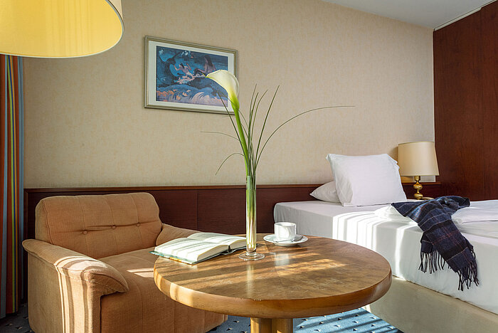 Comfort Zimmer im Maritim Hotel Köln mit gemütlichem Sessel, Beistelltisch, Einzelbett und modernen Dekorationselementen.