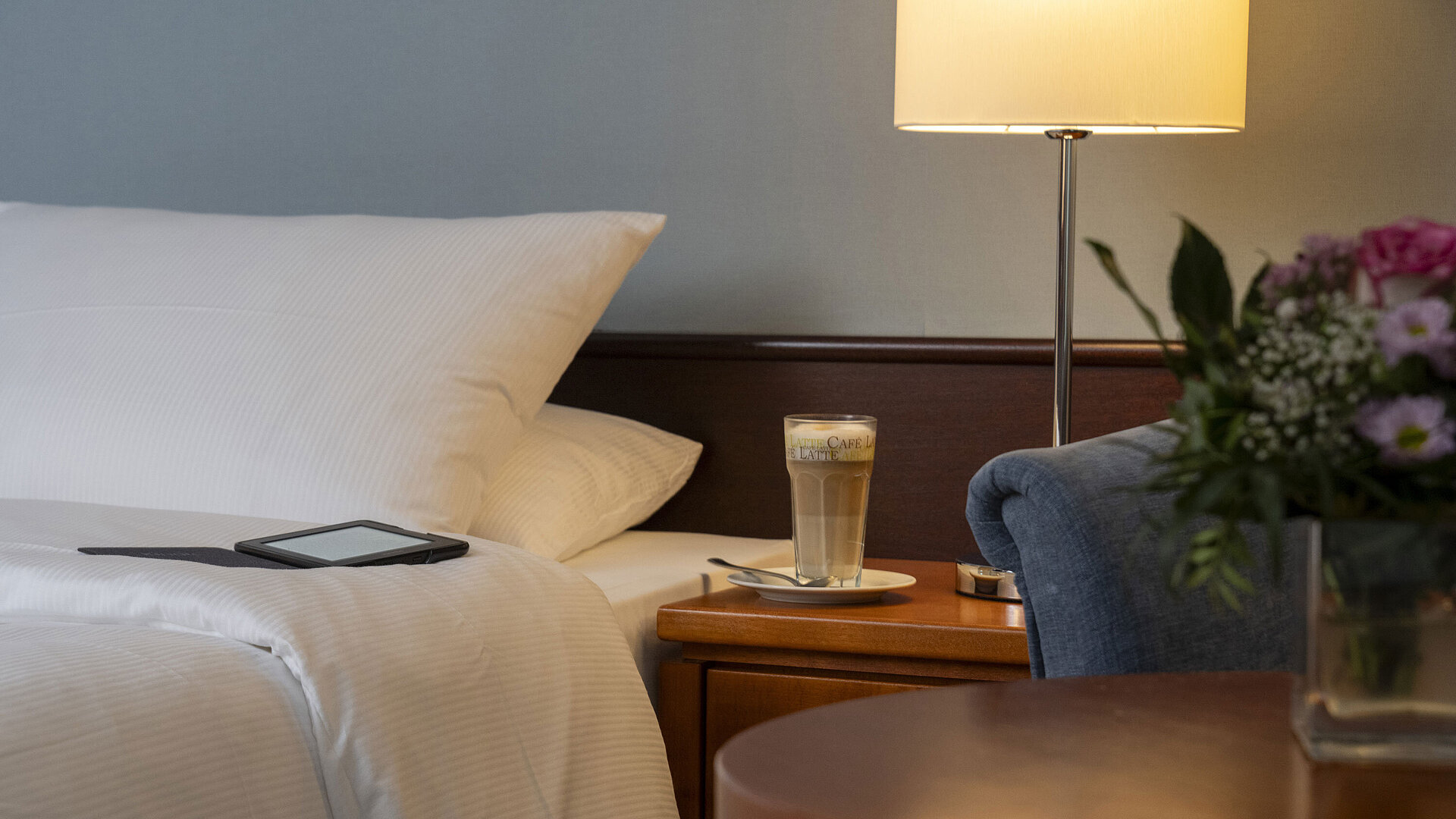 Classic Zimmer Detailaufnahme eines gemütlichen Classic-Zimmers mit Bett, Nachttisch, Latte Macchiato und moderner Beleuchtung.
