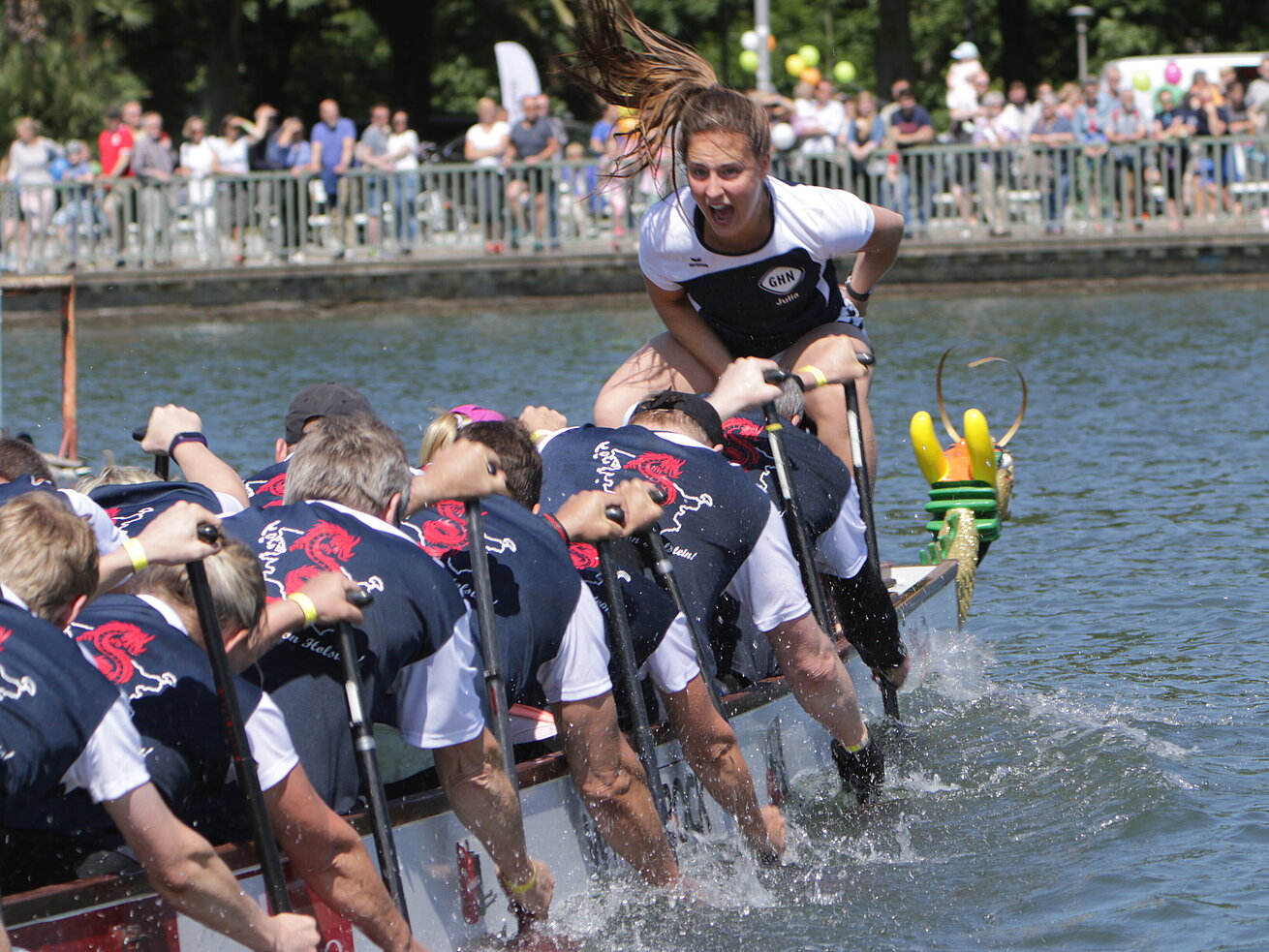 Drachenboot-Team beim Rennen auf dem Fluss mit jubelnder Steuerfrau