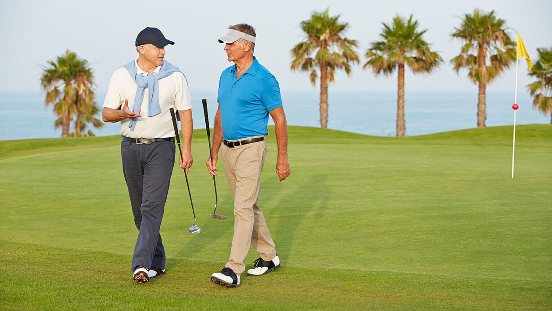 Zwei Golfer gehen über den Golfplatz und unterhalten sich zwischen den Spielbahnen.