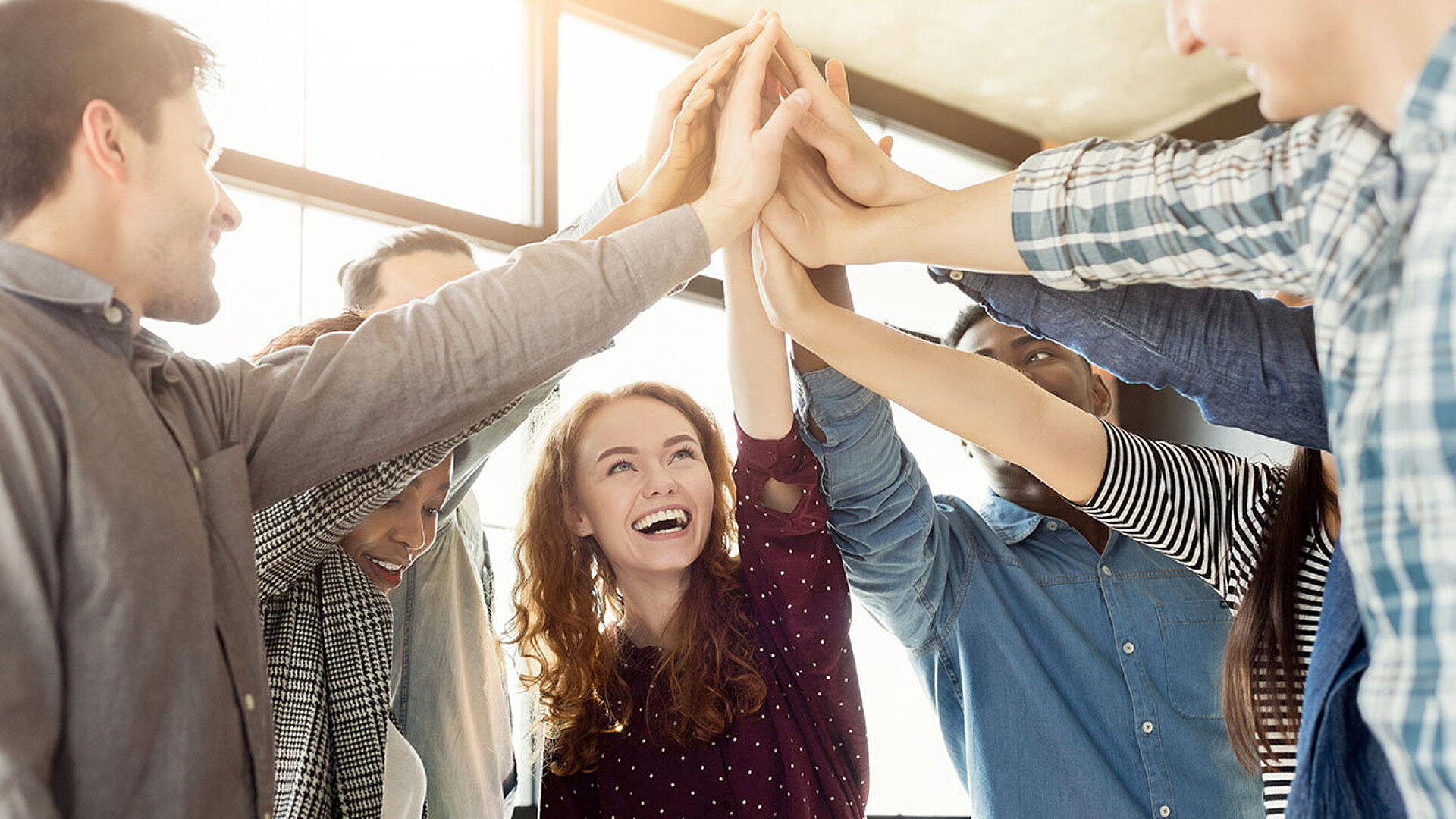 Gruppe von jungen Menschen gibt sich ein High-Five und feiert gemeinsam einen Erfolg.