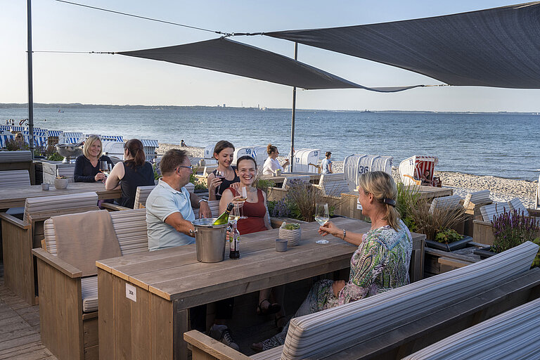 Gruppe von Gästen in der Strandbar des Maritim Seehotel Timmendorfer Strand, genießt Drinks mit Meerblick und Strandkörben.