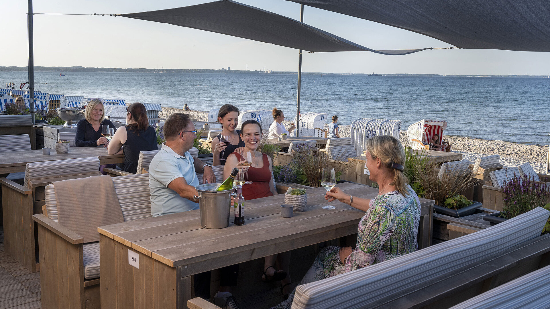 Gruppe von Gästen in der Strandbar des Maritim Seehotel Timmendorfer Strand, genießt Drinks mit Meerblick und Strandkörben.