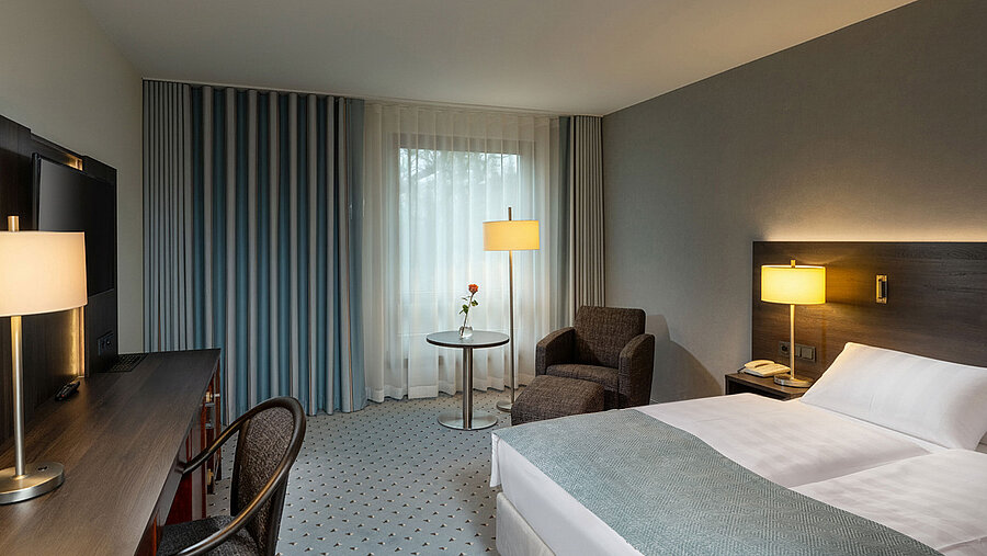 Classic Queen Zimmer mit Queensize-Bett, Sitzbereich, Schreibtisch, warmem Licht und klassischer Einrichtung.