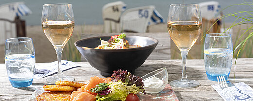 Gedeckter Tisch mit Fischgericht und Wein auf einer Terrasse mit Blick auf das Meer.