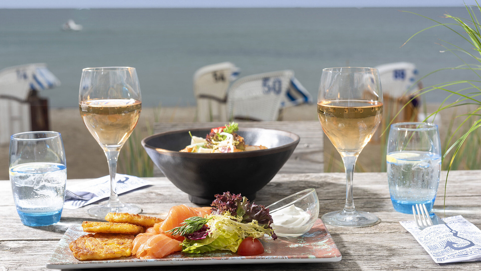 Beach Lounge Gedeckter Tisch mit Fischgericht und Wein auf einer Terrasse mit Blick auf das Meer.